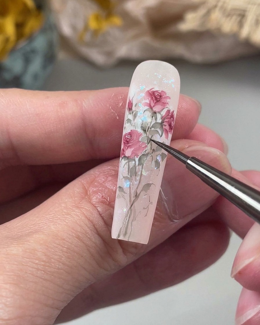 Un pinceau de détail fin dessinant des tiges délicates et légèrement incurvées dans une douce teinte verte, reliant les éléments floraux peints sur longle.