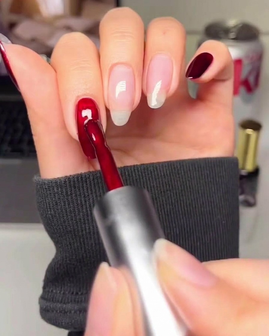 Gros plan dun pinceau appliquant un vernis gel rouge profond et riche sur un ongle préparé.