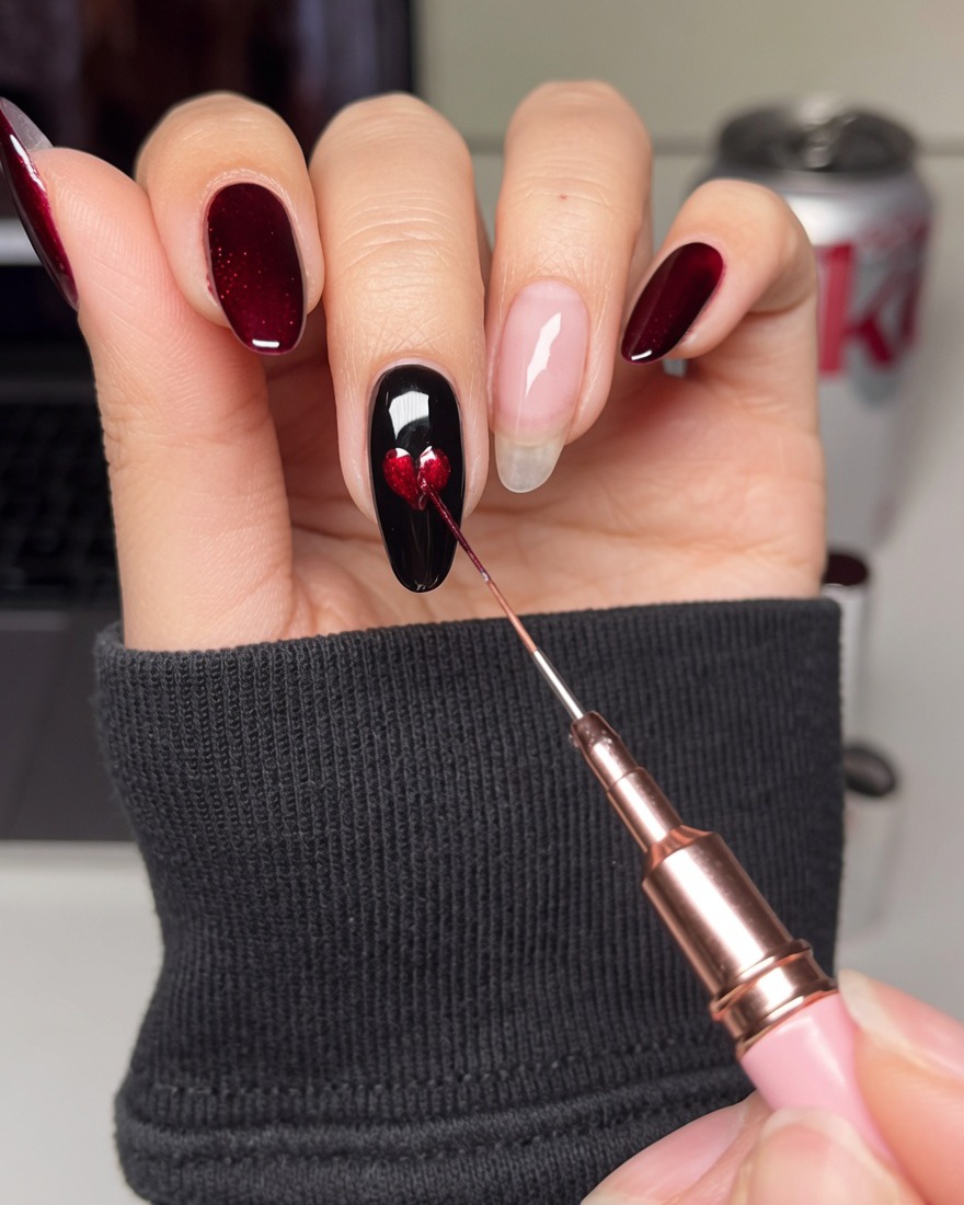Un pinceau de détail fin remplissant le centre dun pochoir en forme de cœur sur un ongle noir avec du vernis gel rouge.