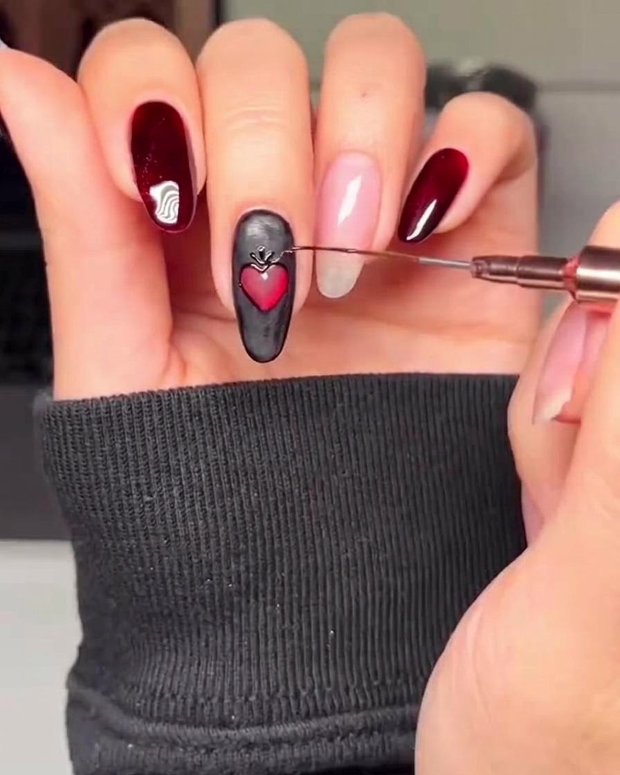 Gros plan dun ongle noir orné dun cœur rouge, avec un pinceau fin ajoutant des accents décoratifs dorés autour du périmètre du cœur.
