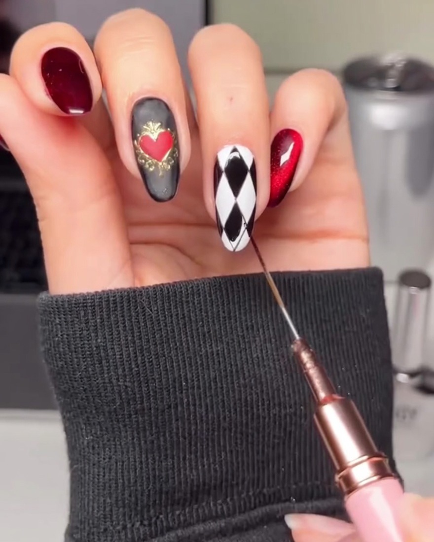 Une main utilisant un pinceau liner pour remplir des losanges alternés sur un ongle blanc avec du gel noir.