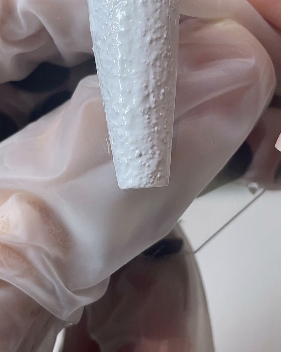 Gros plan sur un pinceau travaillant le gel sable blanc pour créer un bord épais et texturé sur longle.