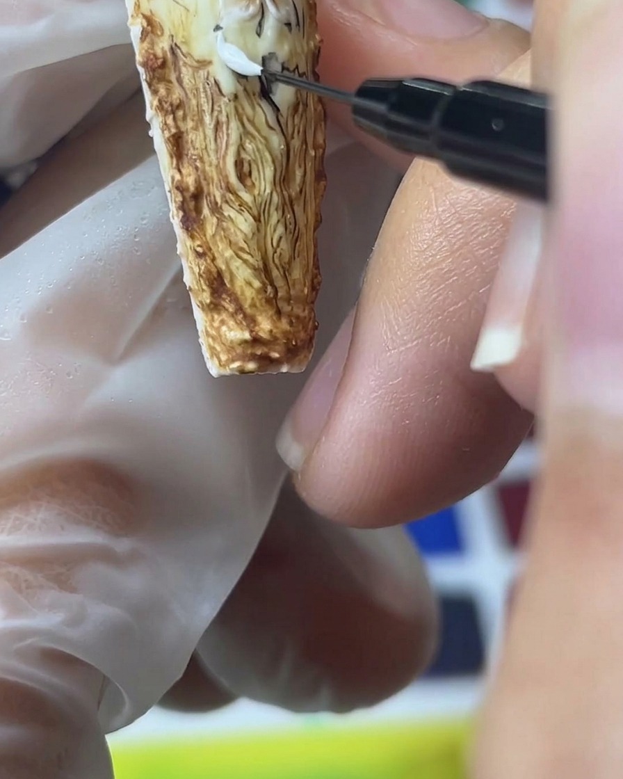 Gros plan dun pinceau de détail appliquant du gel sable blanc pour créer des pétales de rose dimensionnels sur un fond marron.