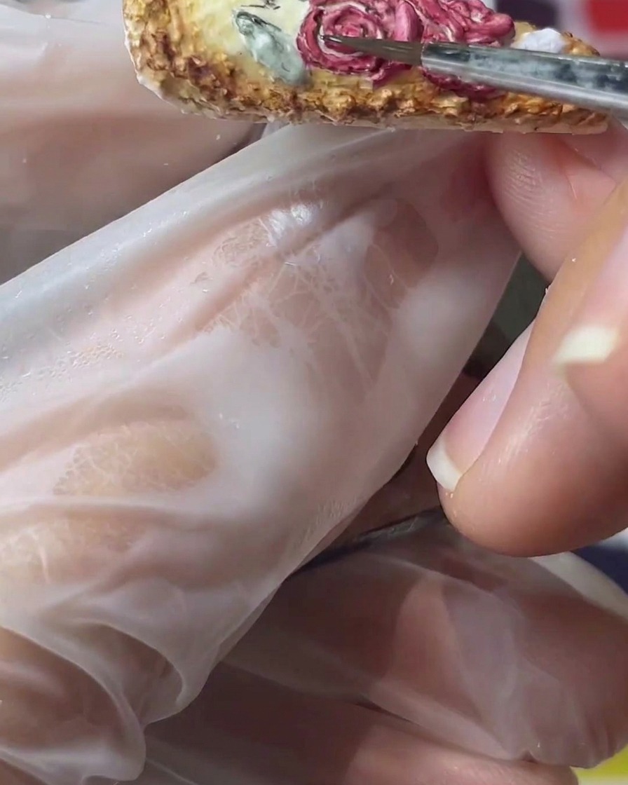 Un pinceau fin peignant des feuilles vert sourd à côté de roses 3D rouges sur un ongle.