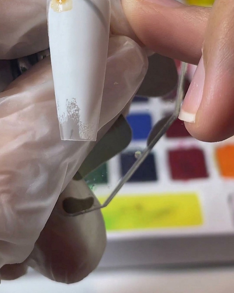 Une main tenant une capsule blanche tout en mélangeant et appliquant des pigments aquarelle marron.