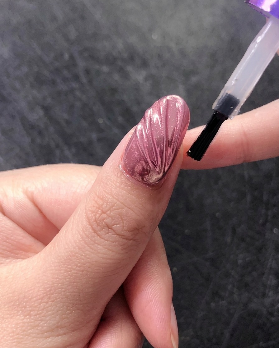 Un pinceau appliquant une couche de finition brillante sur un design dongle coquillage chromé.
