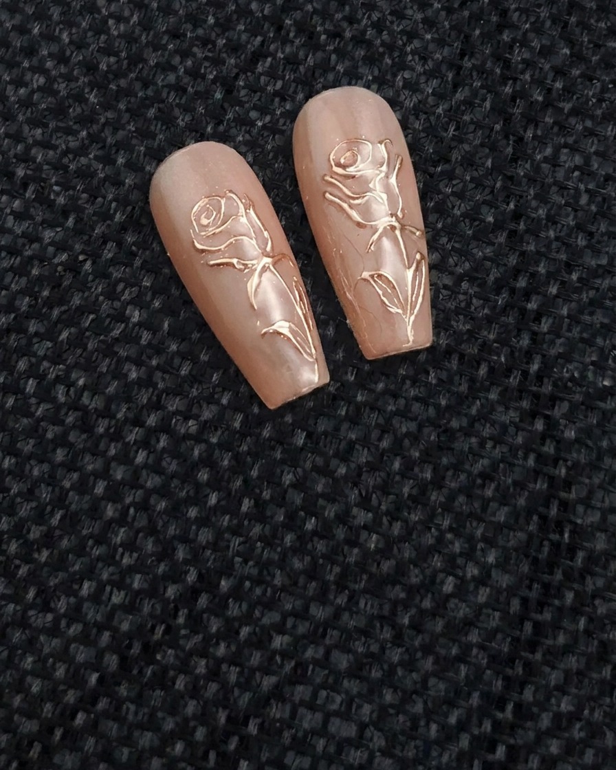 Un pinceau fin pour nail art appliquant un trait de gel transparent en relief en forme de rose sur un ongle nude.