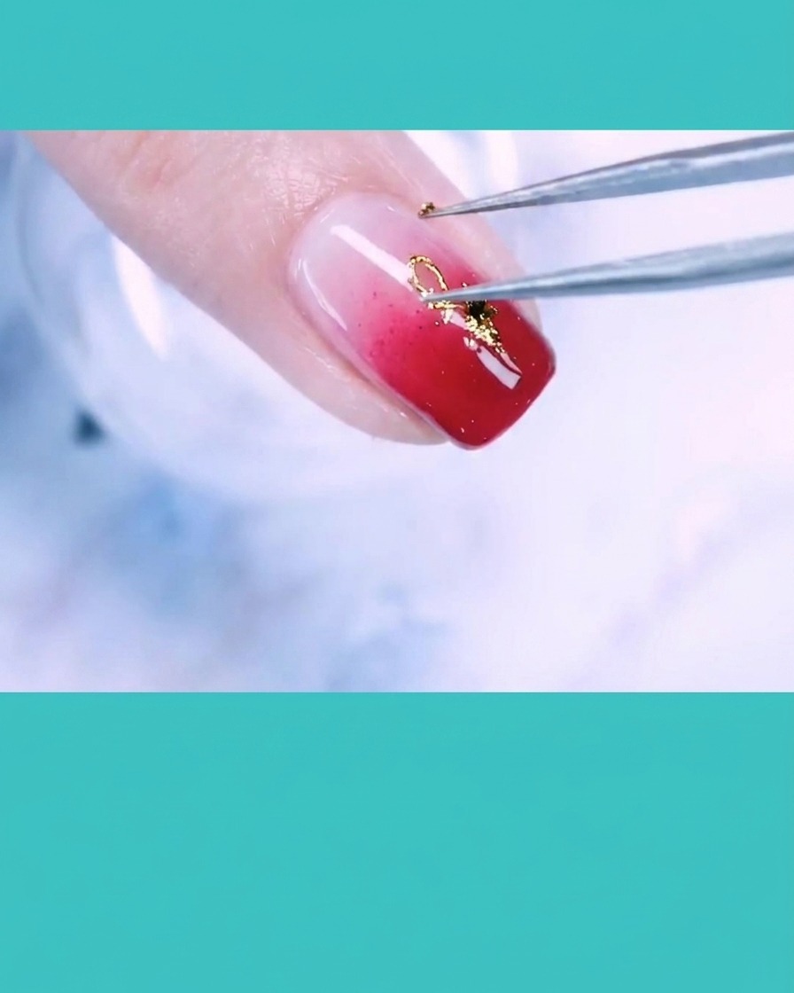 Une pince déposant un petit accent en fil dor sur un ongle décoré de feuilles dor et de perles.