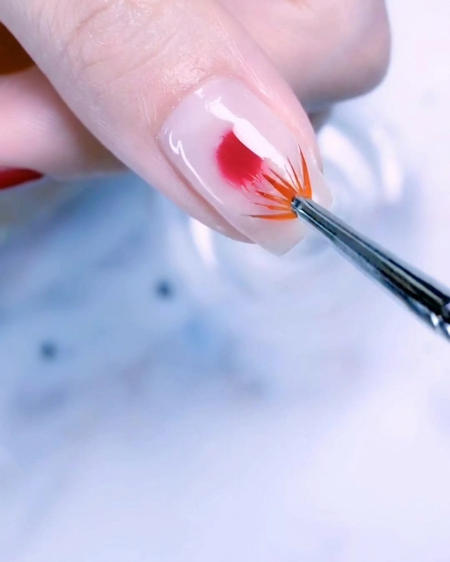 Gros plan dun ongle de pouce avec une base blanc laiteux et une goutte centrale de vernis gel or rose estompée vers lextérieur avec un pinceau éventail.