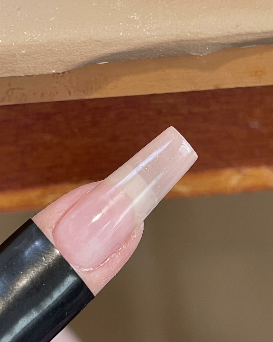 Gros plan dun ongle catalysé sous une petite lampe UV/LED blanche portative.