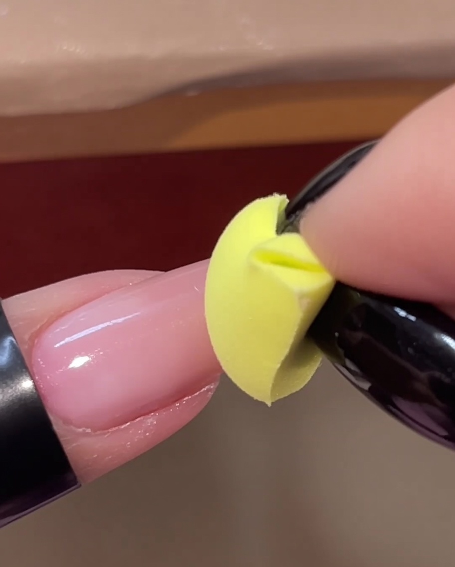 Une éponge jaune tapotant une deuxième couche de gel rose sur le bout dun ongle.