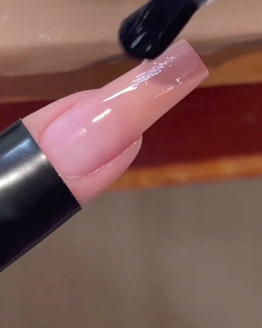 Un pinceau à ongles appliquant un top coat transparent et brillant sur longle fini avec le dégradé rose.