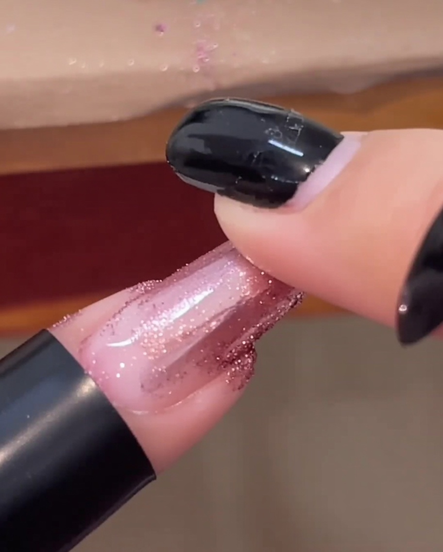 Un bout de doigt frottant de la poudre chrome rose gold sur un ongle fini et brillant.