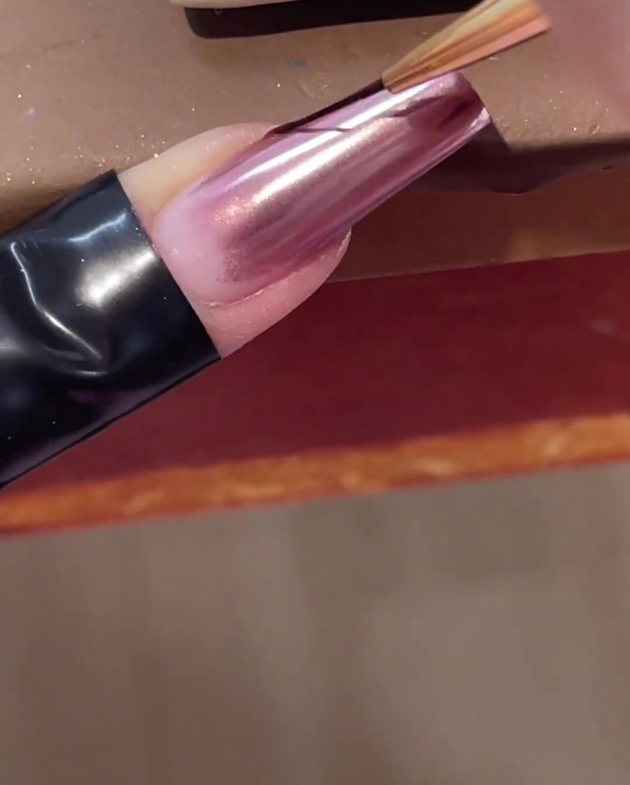 Un pinceau liner fin pour nail art appliquant une ligne de gel de construction transparent en diagonale sur un ongle chromé.