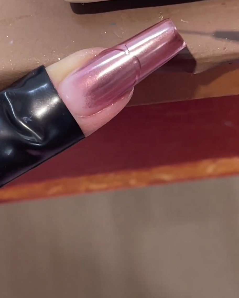 Un pinceau liner fin traçant une ligne de gel transparent en relief sur un ongle chromé rose.