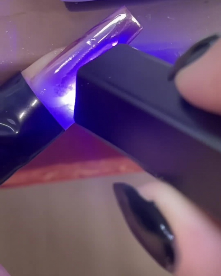 Une mini lampe UV/LED portative catalysant les lignes de gel de construction 3D transparentes sur une extension dongle.