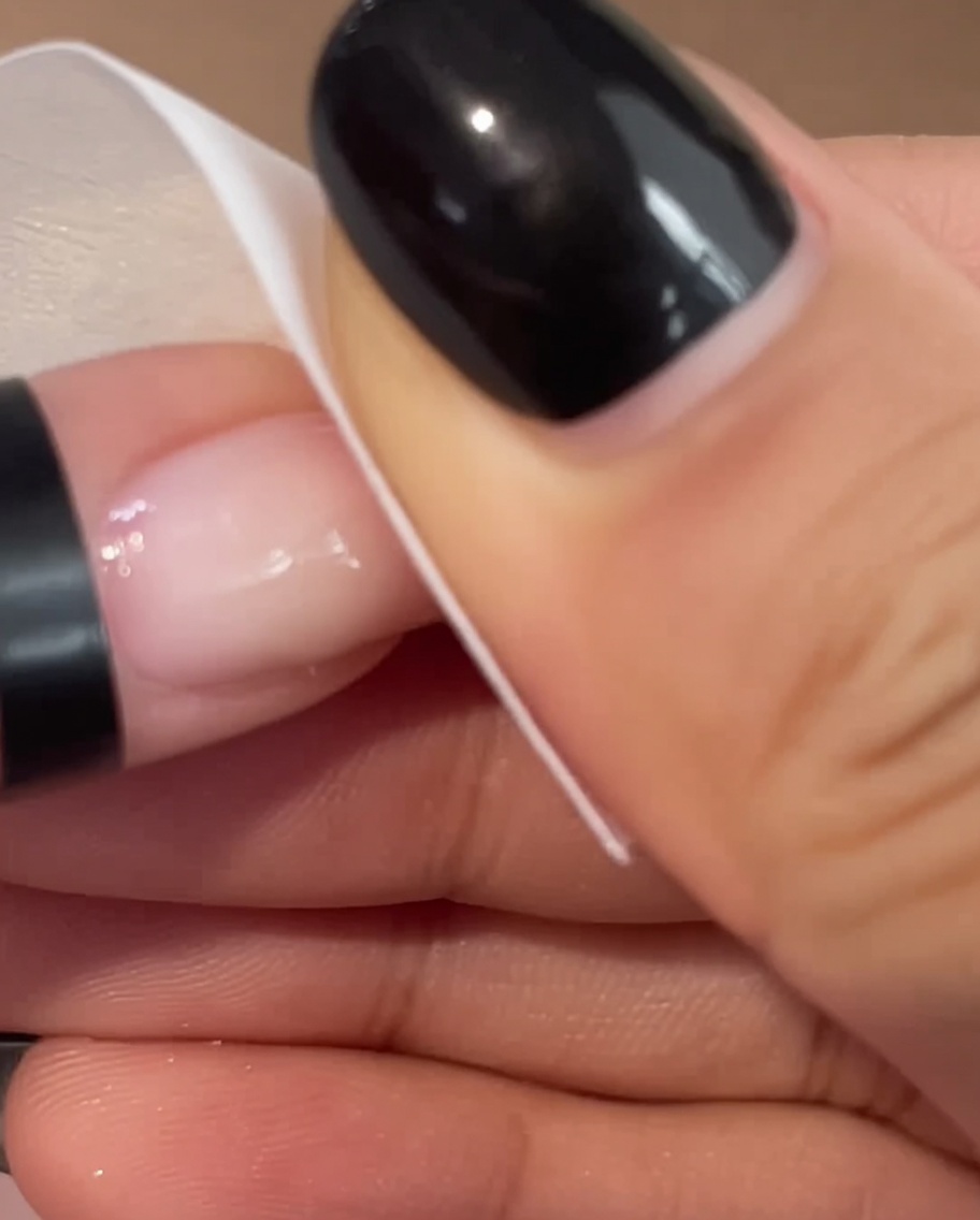 Gros plan dune main utilisant un coton blanc pour nettoyer doucement la surface dun ongle rose manucuré.