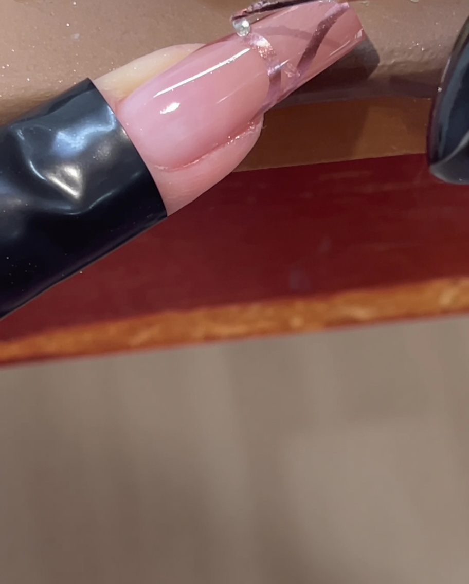 Placement dun petit strass transparent sur une ligne chromée 3D sur un ongle rose à laide dun outil.