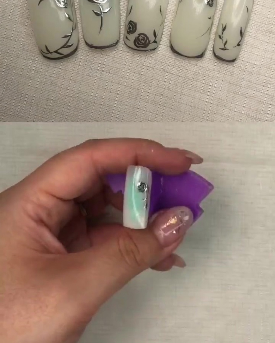 Vue en gros plan du design fini de pétales de rose métalliques sur un ongle blanc, montrant une texture détaillée.