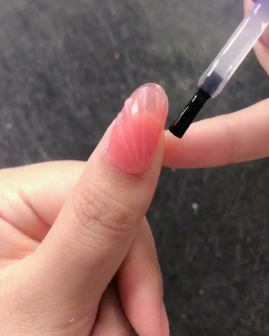 Un pinceau appliquant un top coat transparent, brillant et sans résidu sur le motif coquillage texturé.