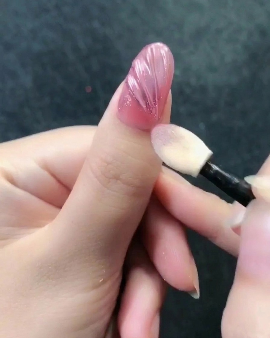 Un applicateur à fard à paupières frottant la poudre chrome or rose sur la surface texturée de longle.