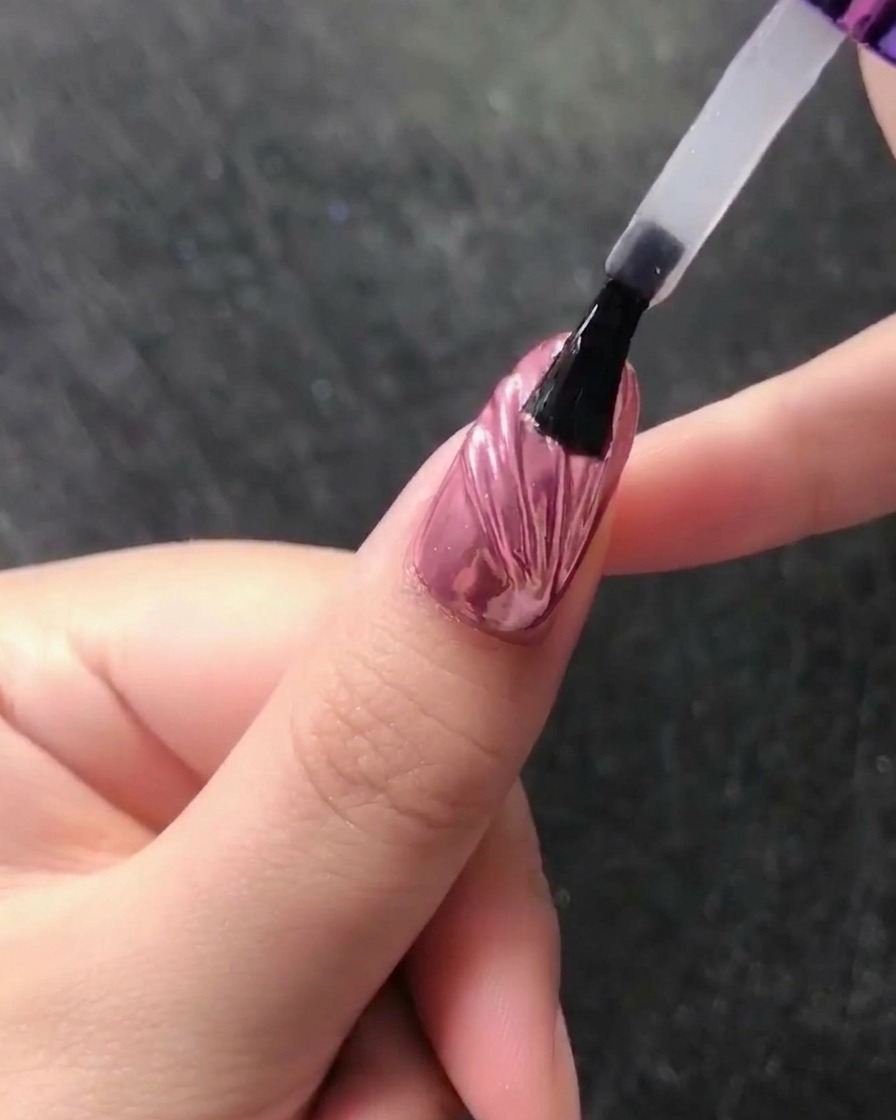 Gros plan dun crayon à cire plaçant une petite perle blanche à la base dun ongle fini au chrome.