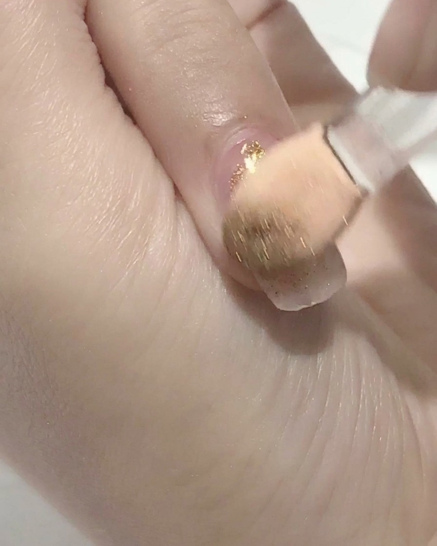 Un pinceau appliquant un top coat transparent sur un ongle en gel rose.