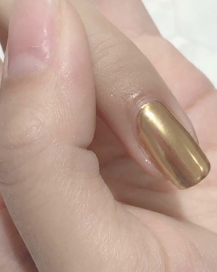 Un applicateur mousse lustrant de la poudre miroir dorée sur un ongle.