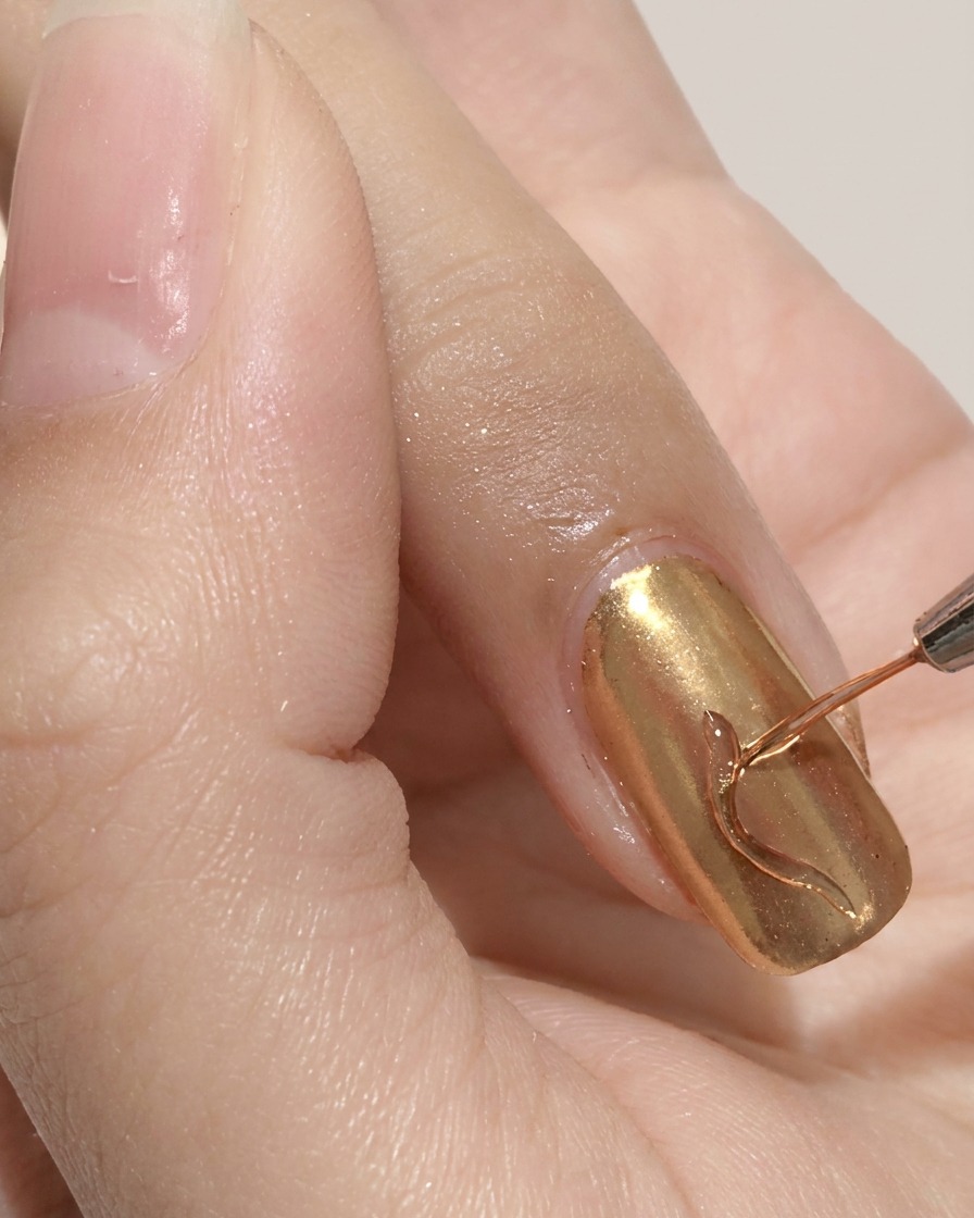 Un pinceau liner fin dessinant une ligne ondulée sur un ongle chromé doré.