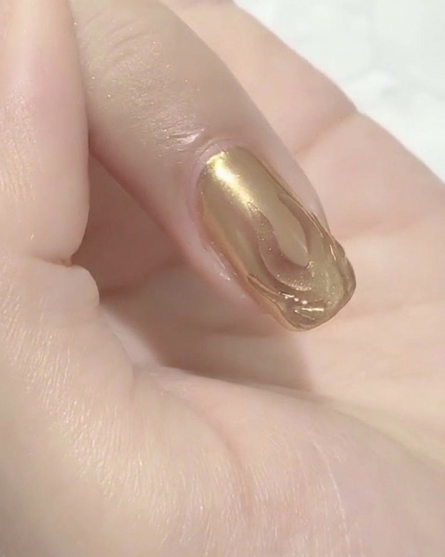 Gros plan sur un coton humide essuyant la surface dun ongle, révélant le motif de flamme métallique défini en dessous.