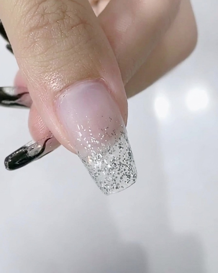 Gros plan dune main avec un dégradé de paillettes argentées sur les ongles à lintérieur dune lampe LED.