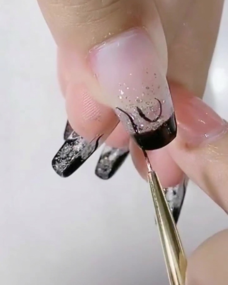 Un pinceau liner ajoutant des courbes noires en S à côté du U central sur un ongle pailleté.
