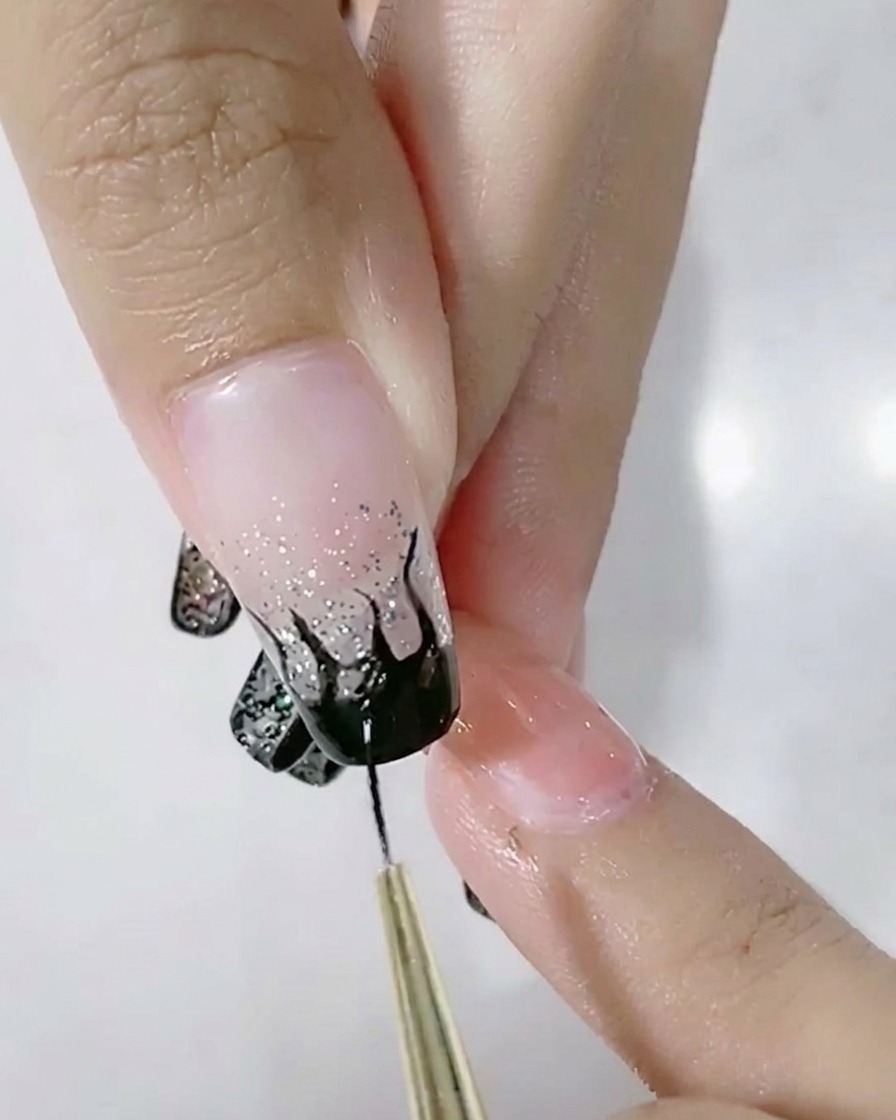 Un pinceau liner remplissant un motif de flamme noire sur un ongle dégradé.