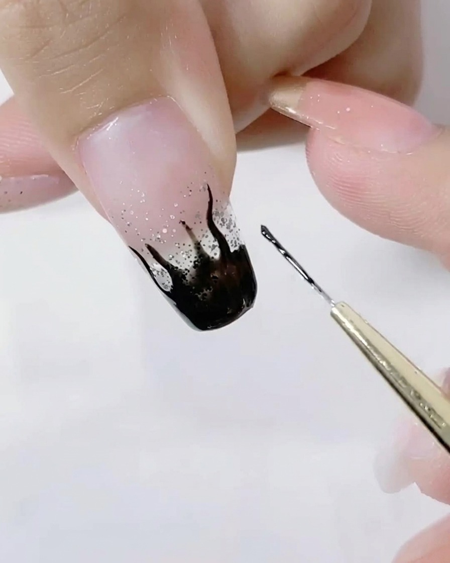 Gros plan dun pinceau liner détaillant les pointes acérées des flammes noires sur un ongle pailleté.