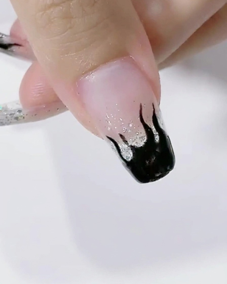 Ongles avec des flammes noires en train de catalyser sous la lumière dune lampe LED.