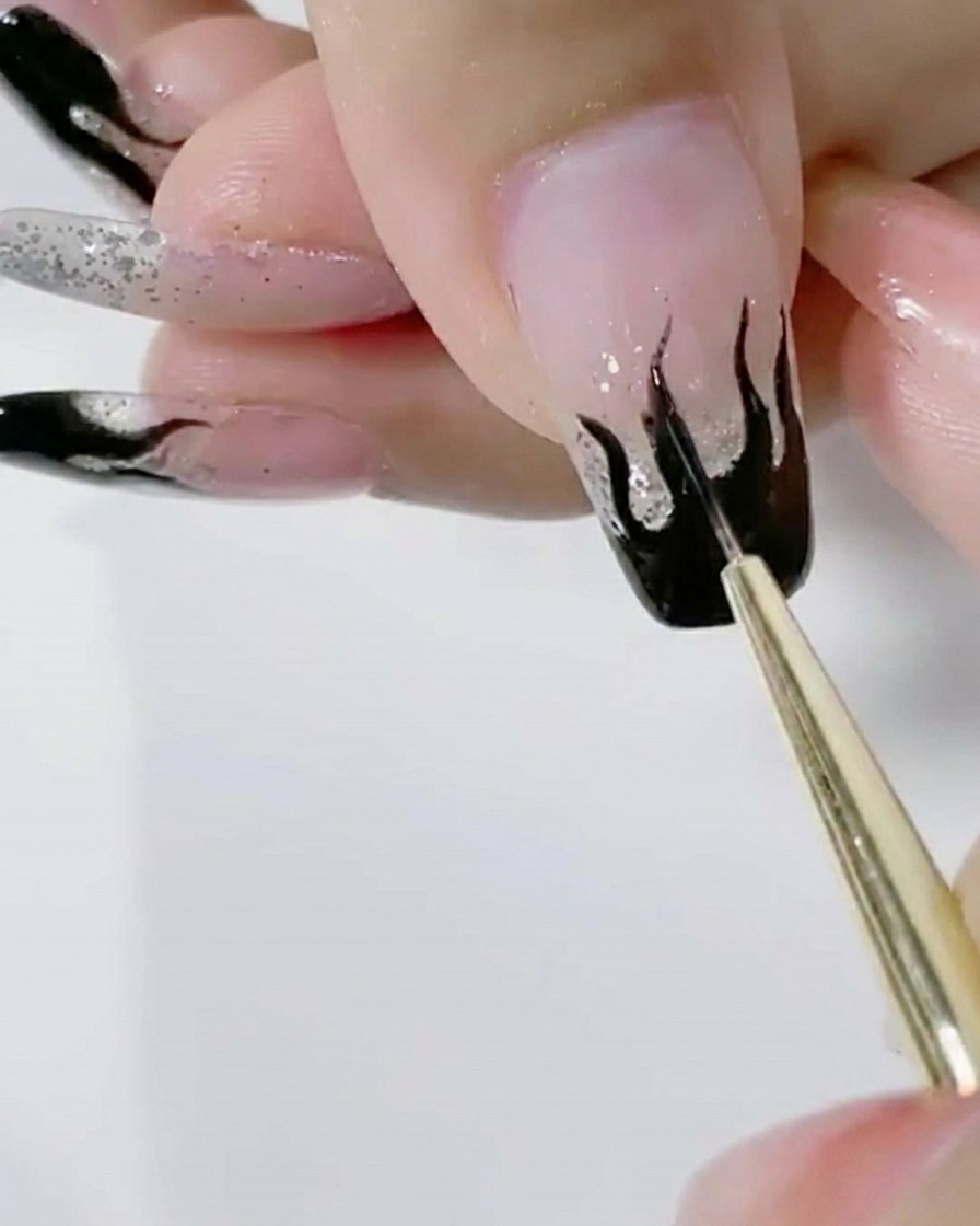 Un pinceau liner appliquant une seconde couche de gel noir saturé sur les flammes.