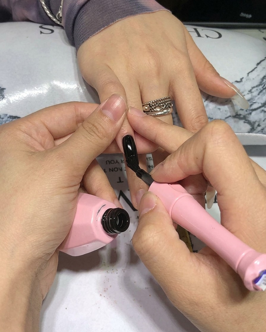 Gros plan dun pinceau appliquant du vernis gel noir sur un ongle naturel.