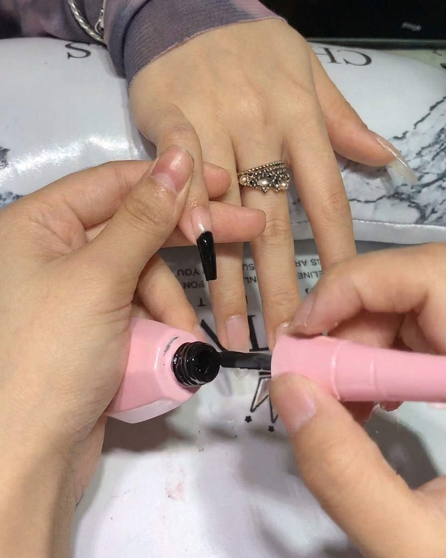 Un pinceau applique une seconde couche de vernis gel noir, révélant une pigmentation intense.