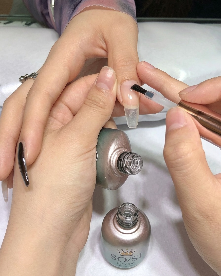 Un pinceau appliquant un top coat transparent sur un ongle peint en noir.