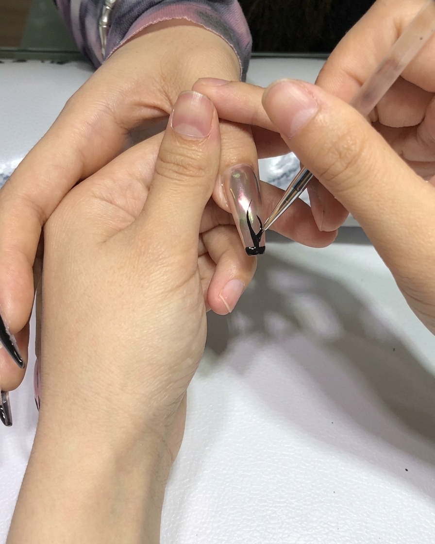 Une main avec le nail art de flammes noires terminé, placée dans une lampe de polymérisation professionnelle pour ongles.