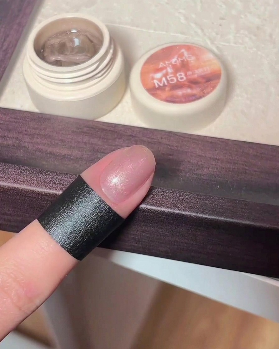 Une main tenant un aimant au-dessus dun ongle en gel fraîchement appliqué, faisant apparaître des reflets de particules magnétiques.