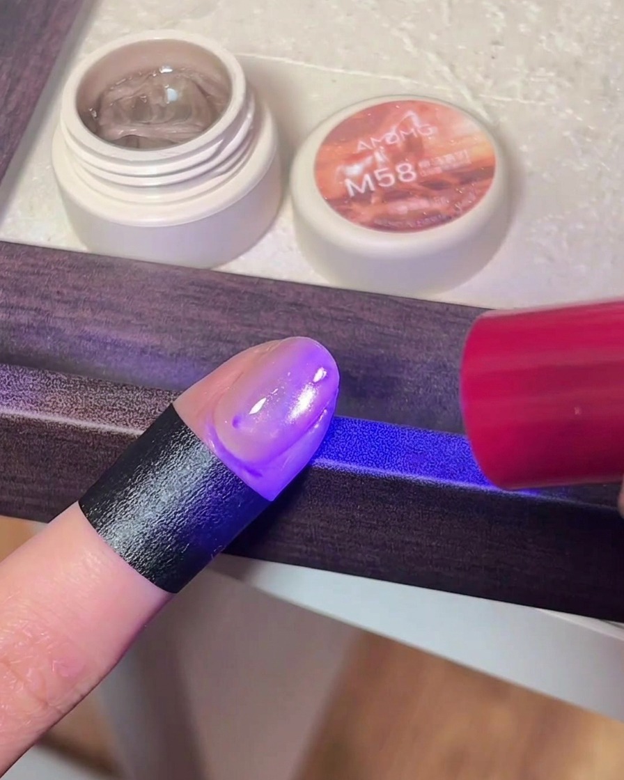 Gros plan dun doigt avec du vernis cat-eye sous la lumière violette dune lampe UV/LED.