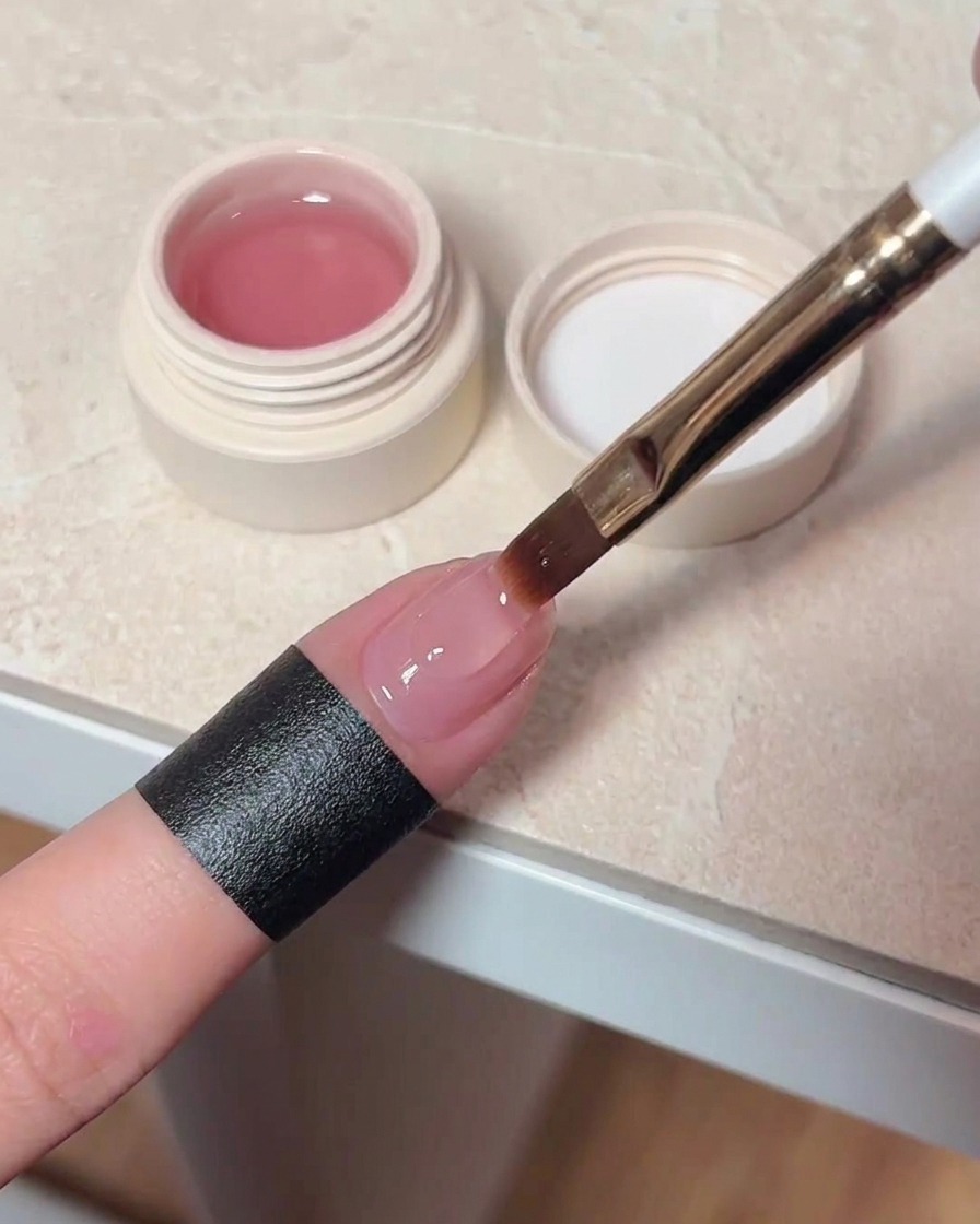 Un pinceau appliquant un top coat transparent et brillant sur un ongle cat-eye catalysé.