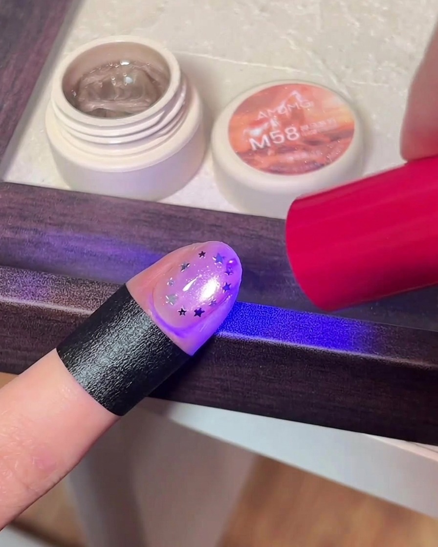 Un doigt avec un nail art étoilé en cours de catalysation sous une lampe UV/LED.