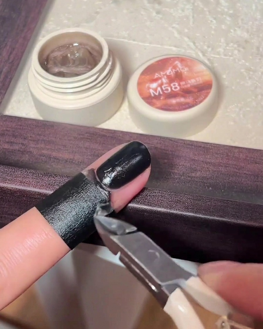 Un petit pinceau de précision appliquant du gel noir sur une breloque croix en relief.