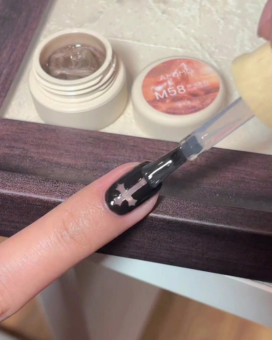 Un pinceau gel appliquant un top coat brillant sur un ongle noir orné dune croix.