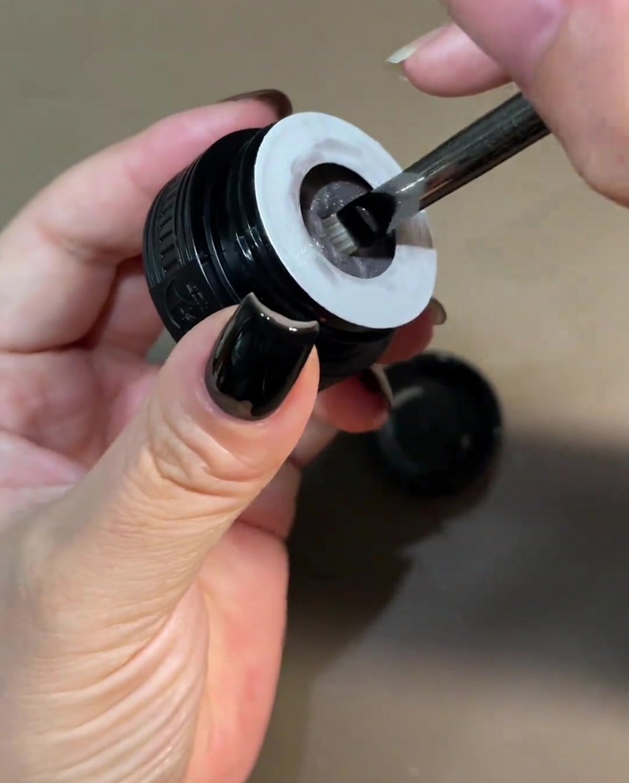 Un petit pinceau plongé dans un pot de gel cat-eye blanc nacré.