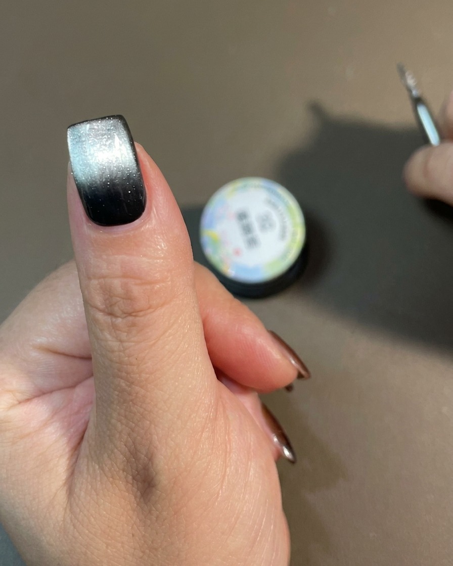 Une main avec un motif de dégradé cat-eye terminé en train de catalyser sous une lampe à ongles.