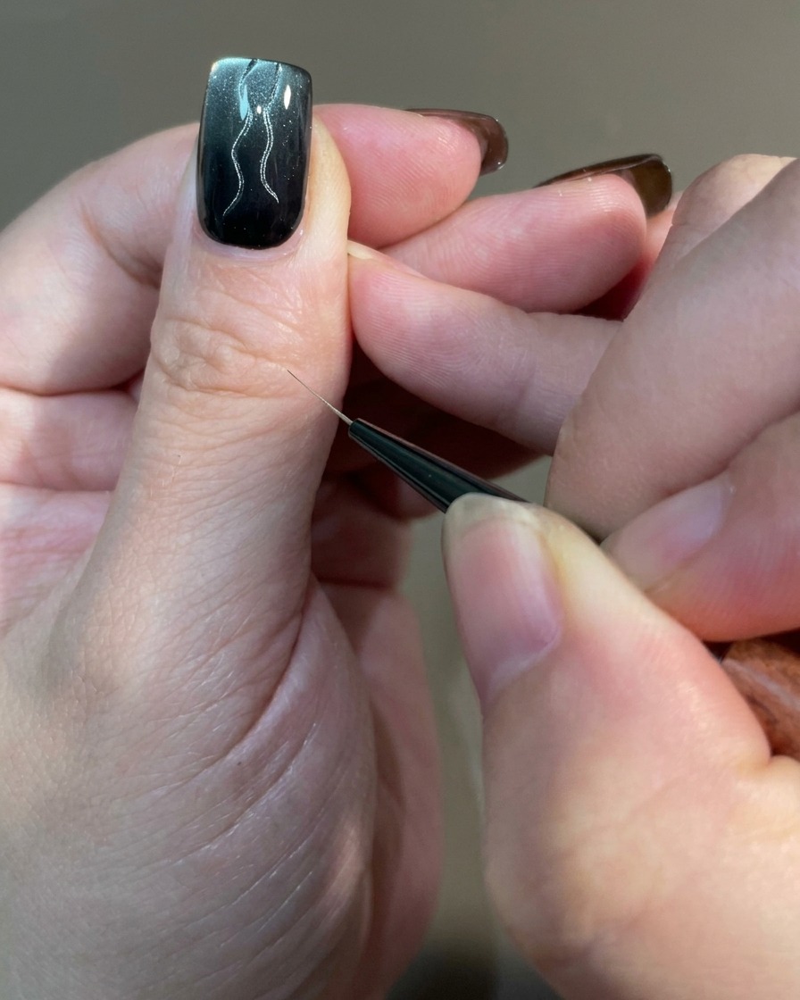 Gros plan dun ongle montrant plusieurs lignes courbes de différentes longueurs tracées avec un pinceau fin sur une base en gel magnétique.