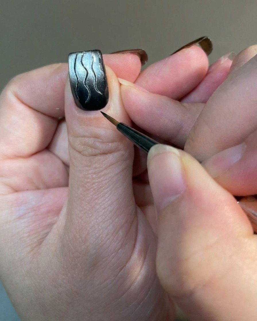 Une photo macro dun pinceau fin ajoutant de petites lignes délicates à la base dun ongle orné de flammes.
